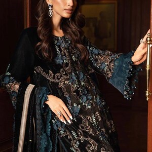 May include: A black velvet dress with intricate floral embroidery in gold and teal. The dress features long sleeves with teal lace cuffs and a matching teal trim. The design includes a long, flowing skirt and a matching shawl.