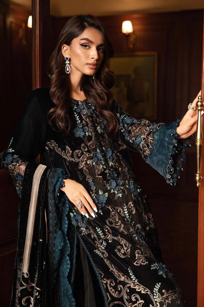 May include: A black velvet dress with intricate floral embroidery in gold and teal. The dress features long sleeves with teal lace cuffs and a matching teal trim. The design includes a long, flowing skirt and a matching shawl.