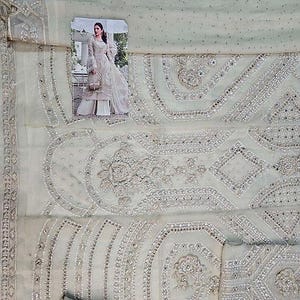 May include: A light green fabric with intricate embroidery and embellishments. The design features floral and geometric patterns, with a small image of a woman in a white dress. The fabric appears to be a delicate material, possibly for a formal outfit.