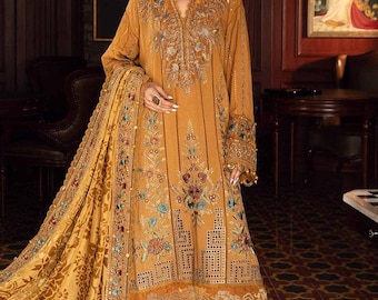 May include: Mustard-colored embroidered dress with intricate floral and geometric patterns. The long-sleeved dress features a V-neck and a matching shawl. The dress is adorned with colorful embroidery and beadwork, creating a luxurious and elegant look.