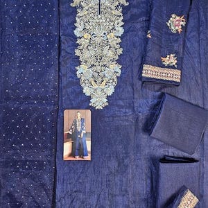 Puede incluir: Un conjunto salwar kameez bordado azul marino. El conjunto incluye una parte superior con intrincados bordados plateados y azul claro, pantalones a juego y una dupatta. Las mangas y el escote presentan patrones florales detallados. Se incluye una peque&ntilde;a foto de una persona que lleva el atuendo.