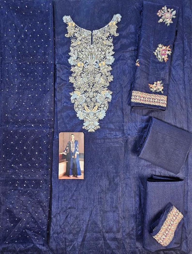 Puede incluir: Un conjunto salwar kameez bordado azul marino. El conjunto incluye una parte superior con intrincados bordados plateados y azul claro, pantalones a juego y una dupatta. Las mangas y el escote presentan patrones florales detallados. Se incluye una peque&ntilde;a foto de una persona que lleva el atuendo.