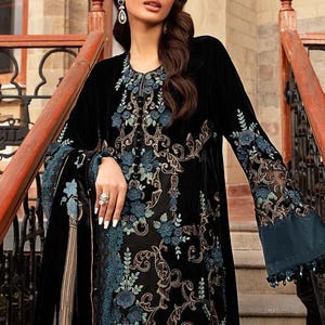 May include: A black velvet dress with intricate floral embroidery in shades of blue and gold. The dress features long sleeves with flared cuffs and a detailed neckline. The design is elegant and suitable for special occasions.