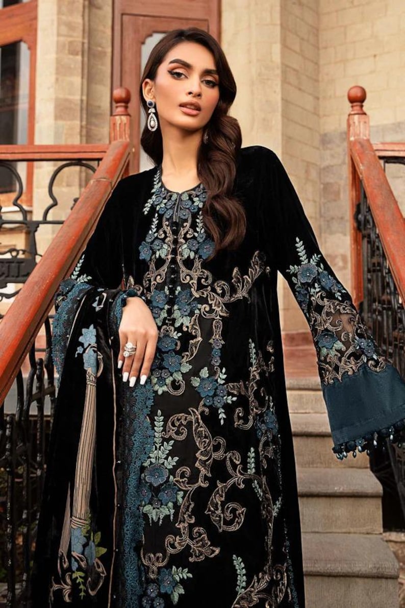 May include: A black velvet dress with intricate floral embroidery in shades of blue and gold. The dress features long sleeves with flared cuffs and a detailed neckline. The design is elegant and suitable for special occasions.
