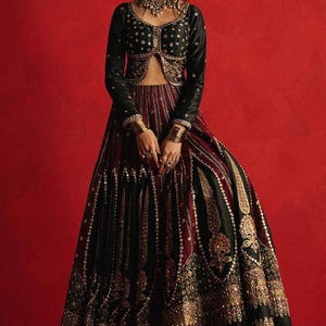 May include: A formal black and burgundy ensemble with intricate gold embroidery. The outfit includes a long-sleeved, cropped black top and a matching floor-length skirt. The skirt features vertical burgundy stripes and ornate gold detailing.