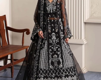 May include: A black formal gown with intricate silver embroidery. The dress features a V-neckline, long sleeves, and a flowing skirt. The design includes floral and geometric patterns. The gown is paired with a matching sheer shawl.
