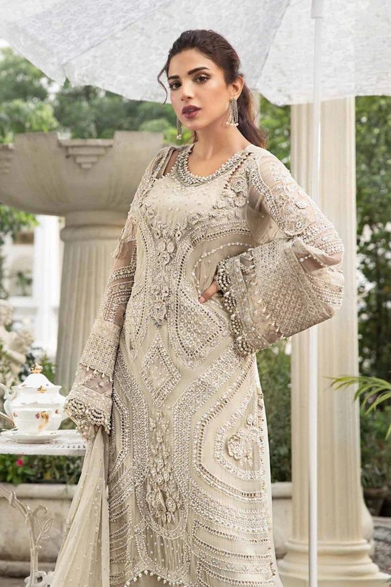 May include: An ivory-colored formal gown with intricate beadwork and embroidery. The dress features long, sheer sleeves with flared cuffs, a detailed bodice, and a flowing skirt. The gown is embellished with pearls and sequins, creating a luxurious look.