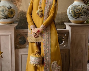 May include: Mustard yellow ensemble featuring a long-sleeved tunic, palazzo pants, and a matching scarf. The outfit is adorned with intricate embroidery in pastel colors. A small, drawstring bag with similar embroidery completes the look. The model is wearing a headpiece and earrings.