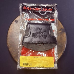 May include: A black leather Safariland belt loop accessory in clear plastic packaging. The item features embossed text including Safariland, Ontario, CA, U.S.A., and 6281 UBS-2.25. A yellow label at the bottom specifies 2.25 inch belt loop size.