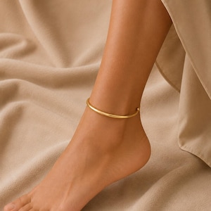 May include: A smooth, polished gold-tone anklet featuring a simple, continuous circular band design. The jewellery piece has a minimalist, solid metallic finish that rests comfortably around the ankle, showcasing a clean and refined aesthetic.