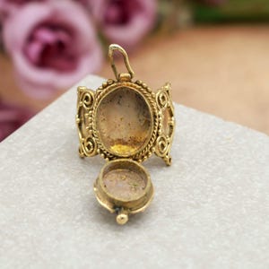 Puede incluir: Colgante de medallón dorado abierto, que revela un compartimento ovalado. El colgante presenta intrincados adornos y un pequeño lazo en la parte superior para una cadena. El diseño es ornamentado y de inspiración vintage, con un cálido tono dorado.
