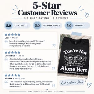 May include: A black sweatshirt featuring a white graphic print of a sun, a globe, and a heart character with the text You're Not Alone Here and HEALING HAPPENS TOGETHER, displayed alongside three five-star customer reviews and a shop rating.