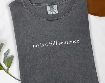 May include: A charcoal grey short-sleeve t-shirt with a crew neckline. The shirt features the white text "no is a full sentence." printed on the chest. A Comfort Colors brand label is visible at the inner neck, indicating a size large.
