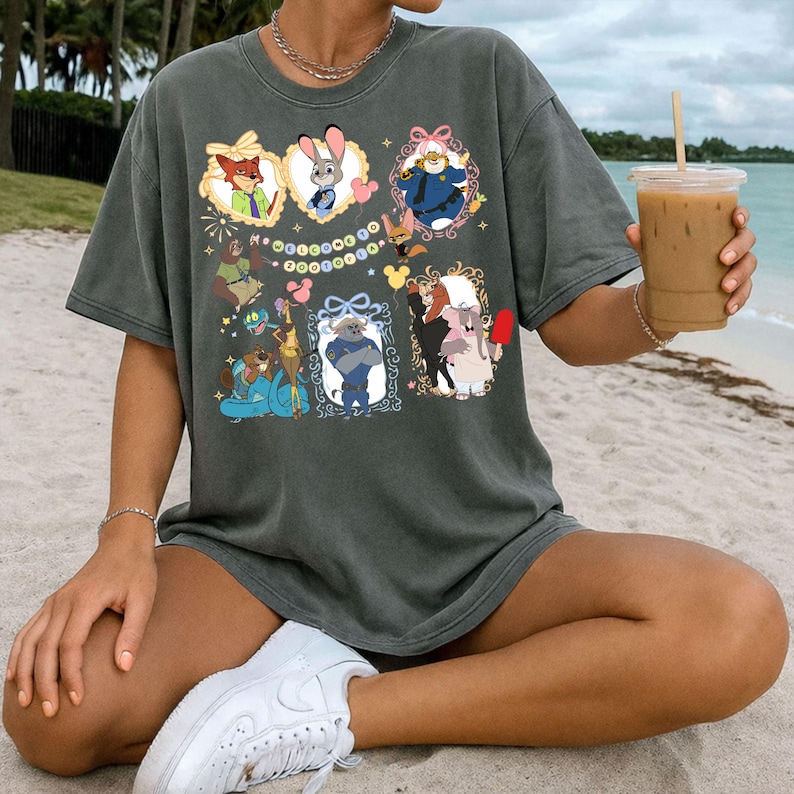 May include: Dark grey t-shirt featuring framed cartoon characters. The shirt showcases characters like a fox, rabbit, and others, set against a beach backdrop. The design includes decorative frames and a string of colourful circles.
