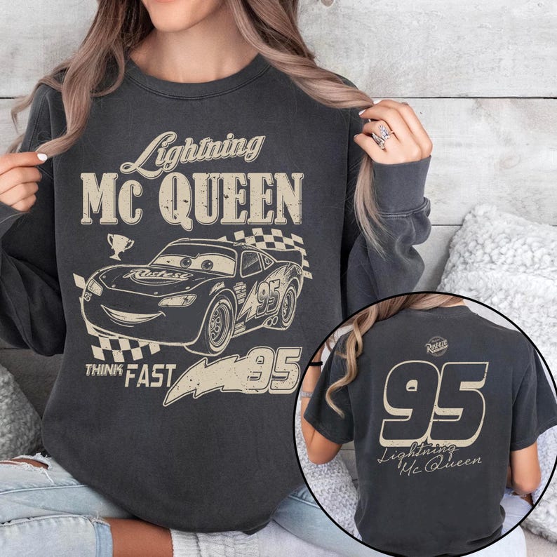 K&ouml;nnte beinhalten: Dunkelgraues Sweatshirt mit Lightning McQueen-Design. Auf der Vorderseite steht "Lightning Mc Queen", ein Bild des Rennwagens, die Nummer "95" und "Think Fast". Auf der R&uuml;ckseite steht die Nummer "95".