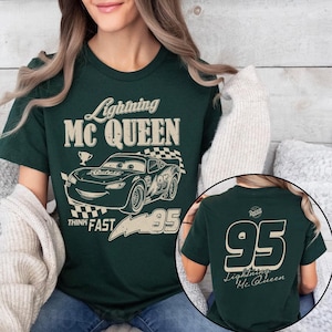 K&ouml;nnte beinhalten: Dunkelgr&uuml;nes T-Shirt mit Lightning McQueen aus dem Film Cars. Das Frontdesign zeigt den Text "Lightning McQUEEN", ein Cartoon-Auto und die Nummer "95". Auf der R&uuml;ckseite des Shirts sind die Nummer "95" und "Lightning Mc Queen" abgebildet.