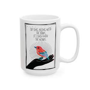 Könnte beinhalten: Weiße Keramiktasse mit einem schwarz umrandeten Design. Das Design zeigt einen bunten Vogel, der auf einer schwarzen Hand sitzt, mit dem Text "I'D SING ALONG WITH THE BIRDS, IF I ONLY KNEW THE WORDS." Die Tasse hat einen großen Henkel.