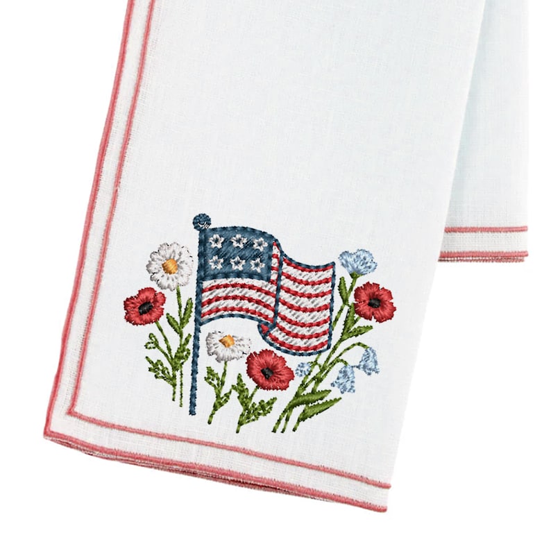 Puede incluir: Toalla de mano blanca con una bandera americana bordada y un dise&ntilde;o floral. La bandera presenta rayas rojas y blancas con estrellas azules. Amapolas rojas, margaritas blancas y flores azules rodean la bandera, con un borde rosa.