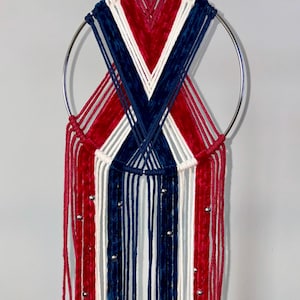 Puede incluir: Adorno de pared hecho a mano con un aro de metal plateado, hilos rojos, blancos y azules. El diseño incluye hebras verticales y un patrón en forma de X, con pequeñas cuentas plateadas. Una pieza decorativa para el hogar.