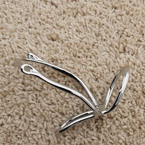 May include: A shiny, silver-colored metal object with a unique, abstract design. The object has a loop and curved lines, possibly a decorative item or a piece of jewelry. The item is set against a neutral, textured background.