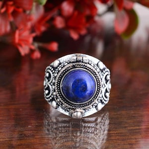 Puede incluir: Un anillo plateado con una piedra grande, redonda y azul oscuro en el centro. El anillo tiene un diseño ornamentado con patrones y texturas detalladas. La piedra está rodeada por un borde trenzado en forma de cuerda. Probablemente sea una joya.