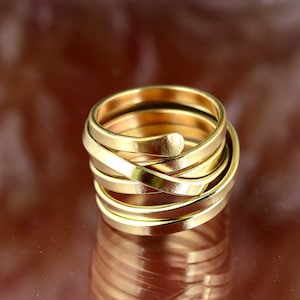 May include: A gold-colored ring with a spiral design. The ring is made of multiple bands that wrap around each other, creating a layered effect. The ring has a smooth, polished finish and reflects light.