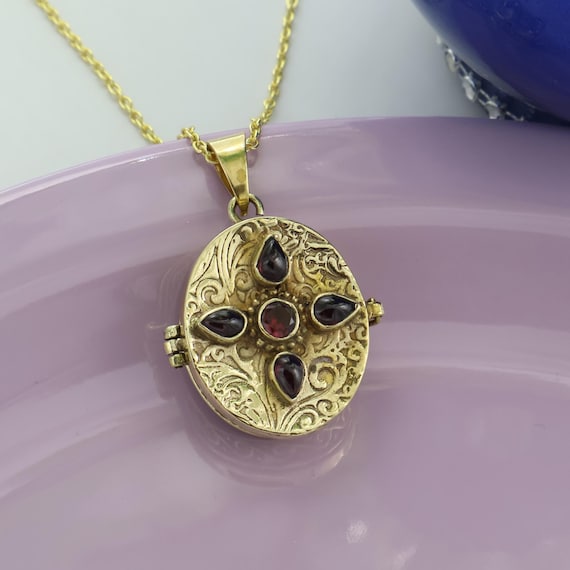 A floral-engraved antique-style gold locket with a genuine garnet stone — 94 favorites confirms real demand for this beautifully crafted keepsake piece.