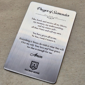 May include: A rectangular, brushed metal card with rounded corners. The card features the text "Prayer of Surrender" at the top, followed by a prayer. The bottom of the card has the word "Amen" and the Sacred Home logo.