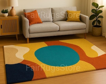 May include: A rectangular rug with a vibrant abstract design. The rug features a large teal circle in the center, surrounded by yellow, orange, beige, and navy blue shapes. The rug is placed on a wooden floor in front of a gray sofa.