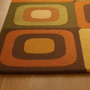 This rug features a retro geometric design with bold, rounded square patterns in warm shades of orange, mustard yellow, olive green, and brown. Its soft texture and mid-century modern style make it a standout piece for any living room or bedroom. The combination of earthy tones and clean, vintage-inspired shapes gives the rug a cozy yet stylish appeal — perfect for adding warmth and personality to your space.