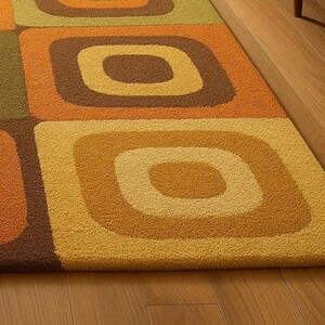 This rug features a retro geometric design with bold, rounded square patterns in warm shades of orange, mustard yellow, olive green, and brown. Its soft texture and mid-century modern style make it a standout piece for any living room or bedroom. The combination of earthy tones and clean, vintage-inspired shapes gives the rug a cozy yet stylish appeal — perfect for adding warmth and personality to your space.