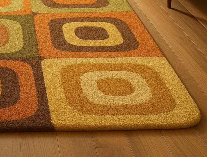 This rug features a retro geometric design with bold, rounded square patterns in warm shades of orange, mustard yellow, olive green, and brown. Its soft texture and mid-century modern style make it a standout piece for any living room or bedroom. The combination of earthy tones and clean, vintage-inspired shapes gives the rug a cozy yet stylish appeal — perfect for adding warmth and personality to your space.