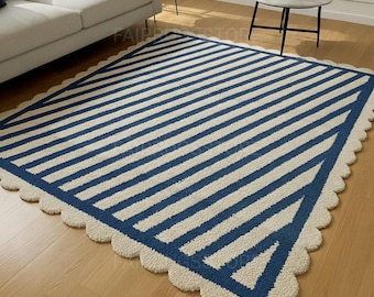 May include: A rectangular rug with a striped pattern in navy blue and off-white. The rug has a scalloped edge and a geometric design in one corner. The rug is placed on a hardwood floor.