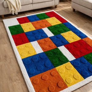 May include: A rectangular rug with a colorful block design. The rug features large, raised blocks in red, blue, yellow, green, and orange, set against a white border. The blocks have a textured, three-dimensional appearance.