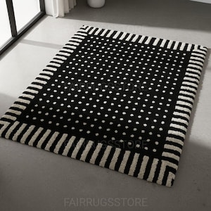 May include: A rectangular black rug with a white polka dot pattern in the center. The border features a white striped design. The rug is placed on a gray floor.