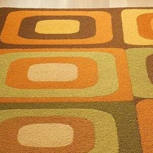 This rug features a retro geometric design with bold, rounded square patterns in warm shades of orange, mustard yellow, olive green, and brown. Its soft texture and mid-century modern style make it a standout piece for any living room or bedroom. The combination of earthy tones and clean, vintage-inspired shapes gives the rug a cozy yet stylish appeal — perfect for adding warmth and personality to your space.