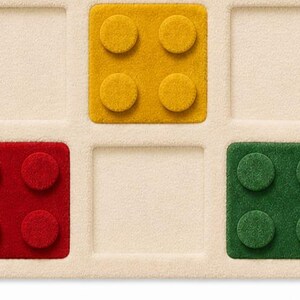 May include: A cream-colored grid board featuring three square, textured game pieces. One yellow piece with four circular studs is in the top center, one red piece with four studs is in the bottom left, and one green piece with four studs is in the bottom right.