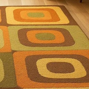 This rug features a retro geometric design with bold, rounded square patterns in warm shades of orange, mustard yellow, olive green, and brown. Its soft texture and mid-century modern style make it a standout piece for any living room or bedroom. The combination of earthy tones and clean, vintage-inspired shapes gives the rug a cozy yet stylish appeal — perfect for adding warmth and personality to your space.