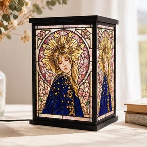 May include: Black rectangular lamp with stained glass panels. The panels feature a woman with long blonde hair, wearing a blue cape with gold stars, and a gold crown. The background is pink and purple with floral designs.