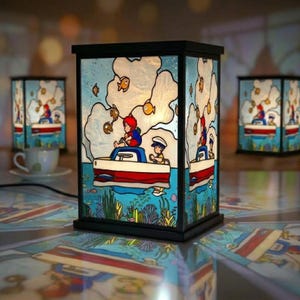 May include: A decorative lamp with a black frame and stained glass panels. The panels depict a cartoon scene of a boat with two people and fish in a blue ocean. The lamp is on a reflective surface, with two other lamps and a teacup in the background.