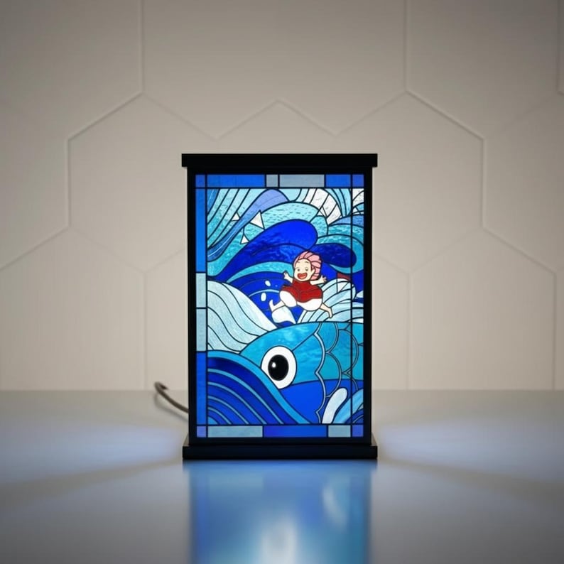 May include: A stained glass lamp featuring a vibrant blue ocean scene with a cartoon character in a red outfit. The lamp has a black frame and base, and the image is illuminated from within.