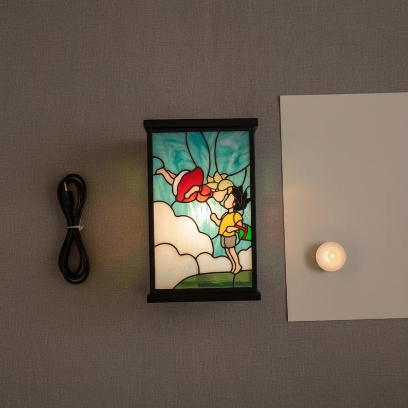 May include: A rectangular stained glass lamp with a black frame. The lamp features a colorful illustration of two children. One child is wearing a red dress and the other is wearing a yellow shirt. A black power cord is to the left of the lamp.