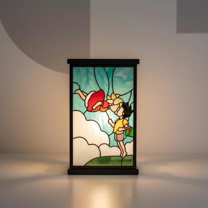 May include: A stained glass lamp featuring a cartoon scene of a boy and girl. The boy wears a yellow shirt and shorts, holding a green bag. The girl wears a red dress. The background is blue and white with a black frame.