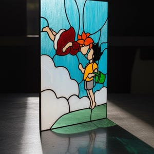 May include: Stained glass panel featuring a whimsical scene of two cartoon figures in a blue sky with white clouds. One figure is wearing a red dress, and the other is wearing a yellow shirt and holding a green bucket. The panel has a black border.