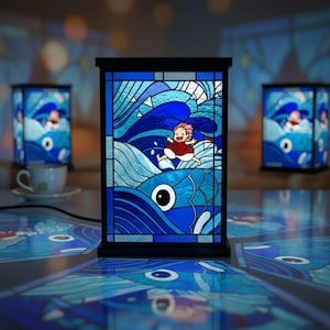 May include: A stained glass lamp with a black frame, featuring a vibrant blue ocean scene with a running figure and a large fish. The lamp is illuminated, with two similar lamps in the background. The scene is reminiscent of a popular animated film.