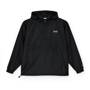 May include: Black anorak jacket with a hood and a half-zip closure. The word "feral" is printed in white on the chest. Features a front pocket and a drawstring at the hem. The Champion logo is visible on the sleeve.
