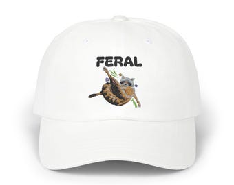 May include: White baseball cap with the word "FERAL" in black block letters. The cap features an embroidered raccoon illustration with floral accents. The raccoon is brown, gray, and tan.