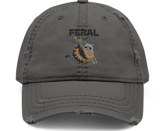 May include: Distressed gray baseball cap with the word "FERAL" embroidered above an image of a raccoon hanging from a branch. The raccoon is brown, white, and gray, with green leaves. The cap has a pre-worn look.