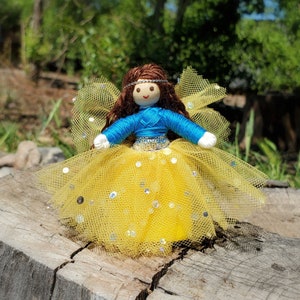 May include: A handmade doll with brown hair, blue eyes, and a blue and yellow dress. The doll is wearing a yellow tulle skirt with silver glitter.