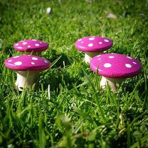 May include: Five pink and white mushroom shaped decorations with white polka dots. The mushrooms are sitting on a bed of green grass.